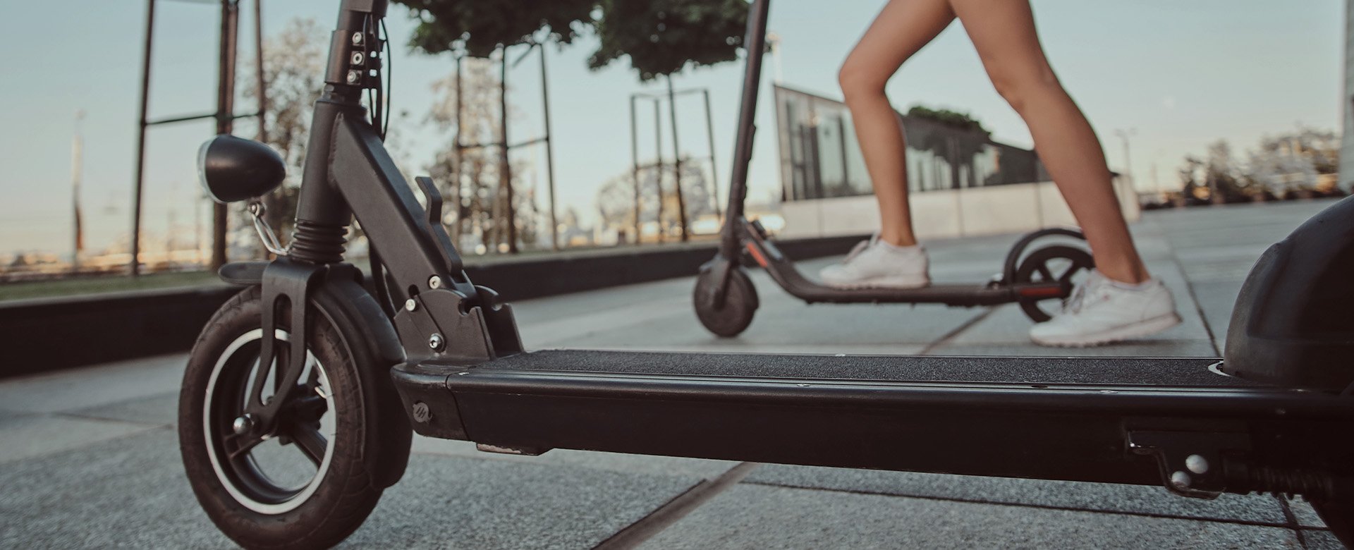 Elektrické kolobežky pripravené na jazdu po meste. Na jednu z nich práve naskakuje žena chystajúca sa vyraziť.