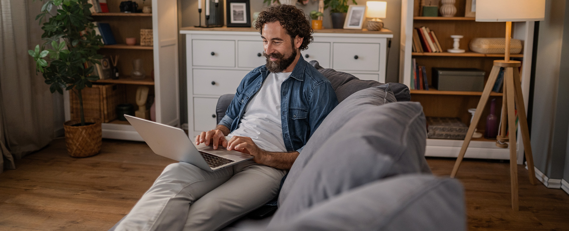 Muž v domácom prostredí sa s úsmevom pozerá do notebooku.