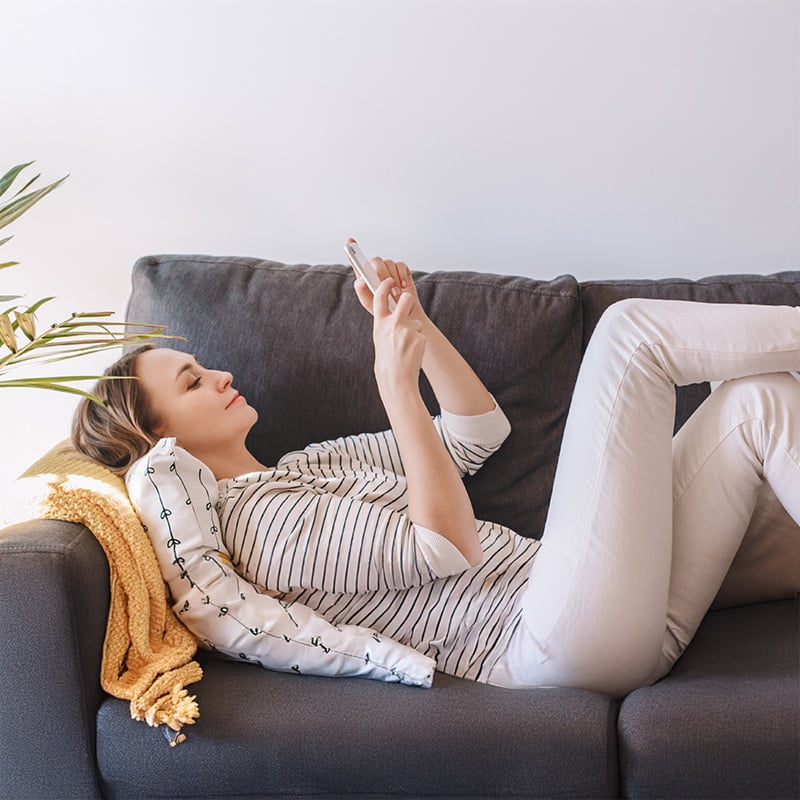 A woman lying on a couch, looking at her phone.