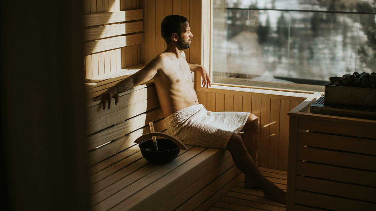  Muž si vychutnáva saunu, pozerá sa z okna na zasneženú krajinu.