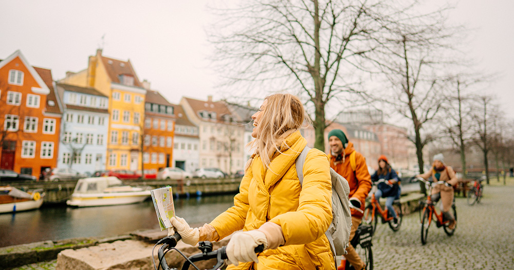 Partia ľudí sa bicykluje popri rieke a farebných budovách.