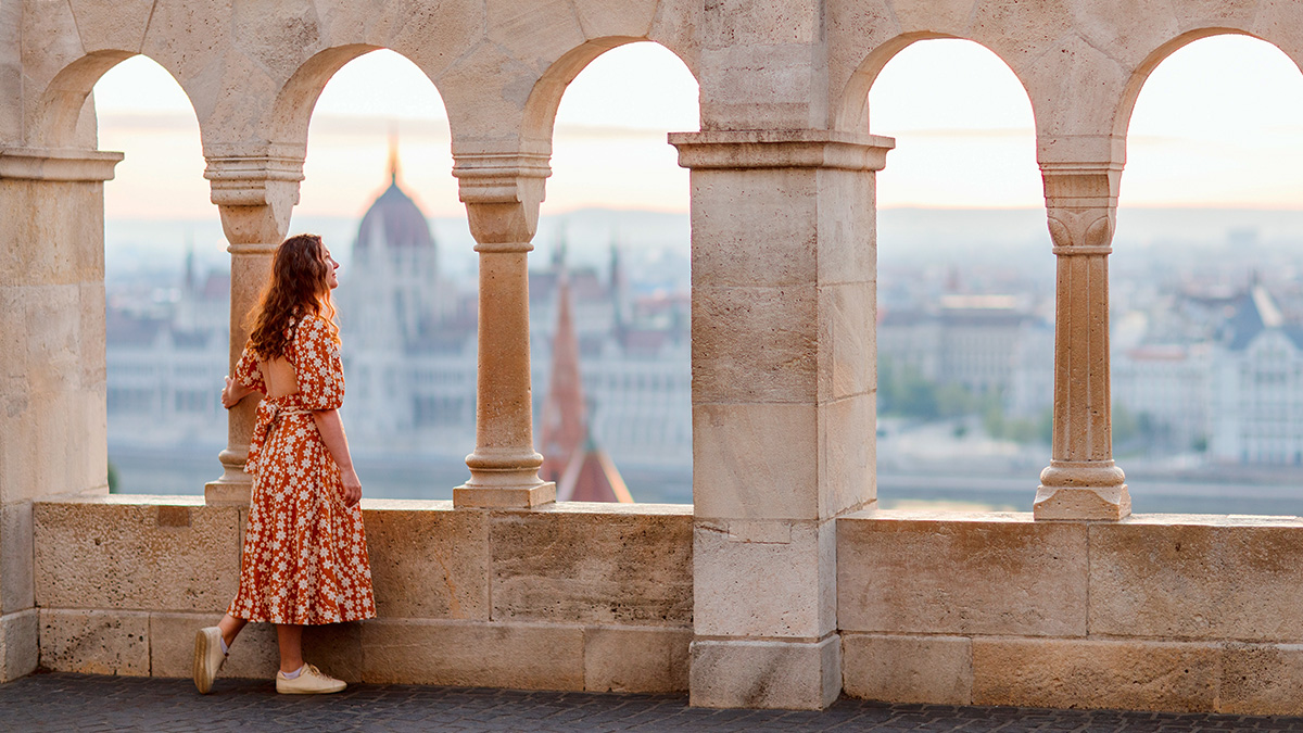 Turistka sa pomedzi historické piliere a oblúky pozerá na Budapešť.