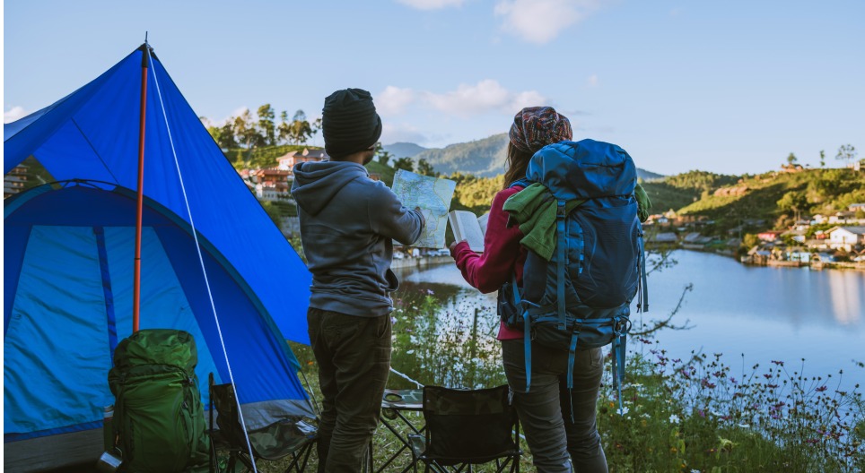 Dvaja ľudia s ruksakmi pozerajú do mapy vedľa stanu.