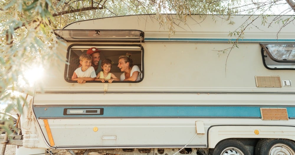 Rodičia s detmi pozerajú von z okna karavanu.