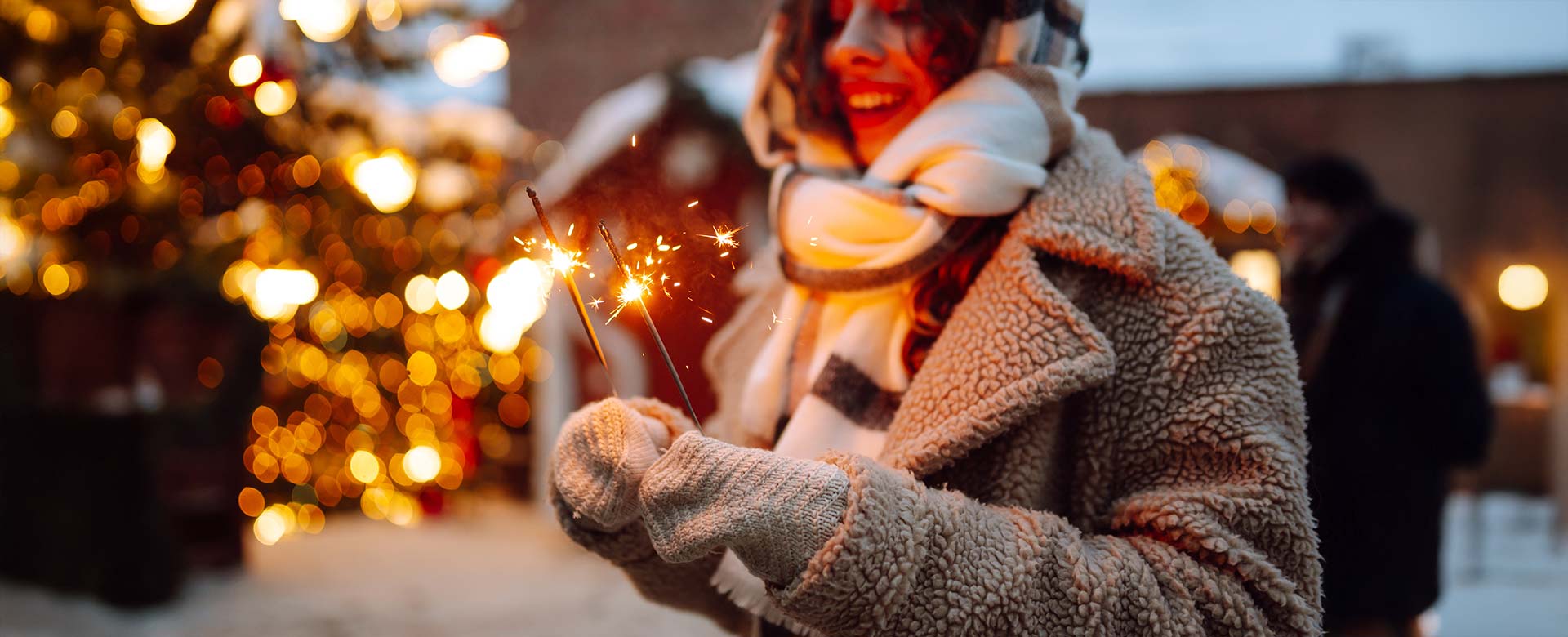 Dievča zababušené v teplom kabáte a veľkom šále drží v rukách zapálené prskavky.