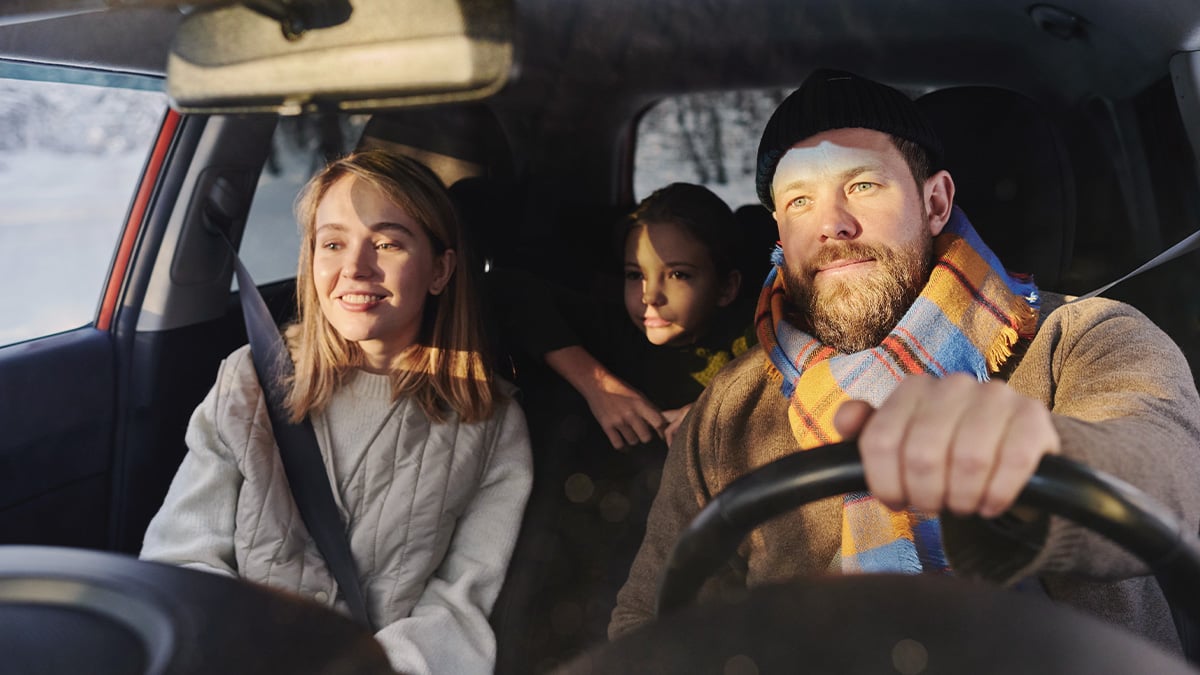 Záber na posádku auta. Muž, žena a dieťa pozerajú uprene pred seba na cestu. 