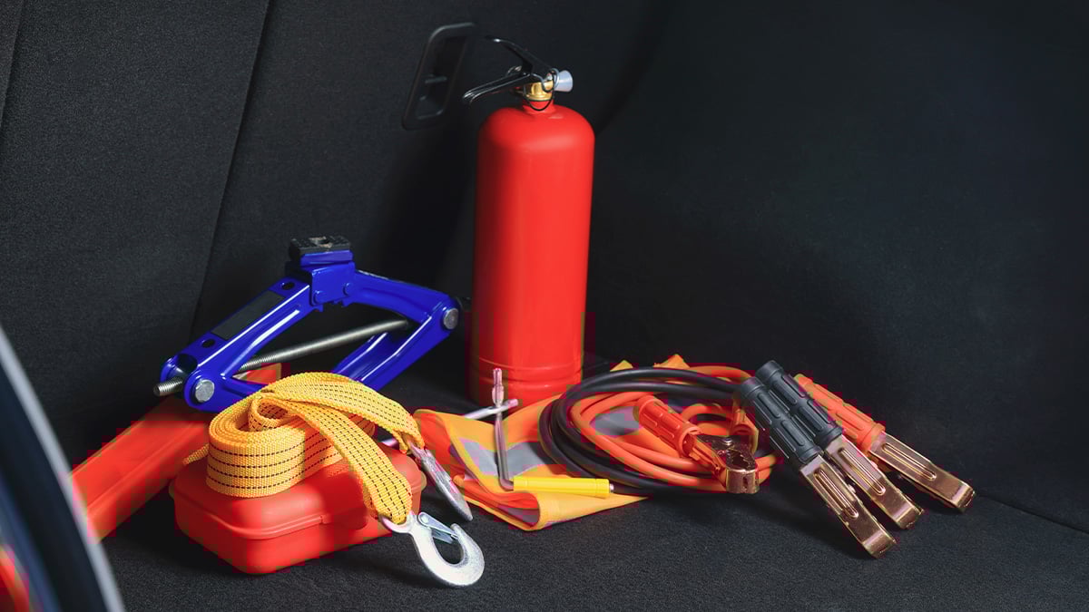 Otvorený kufor auta, v ktorom je hasiaci prístroj, štartovacie káble, lekárnička, reflexná vesta a ďalšie predmety, ktoré pomôžu vodičom v núdzovej situácii.