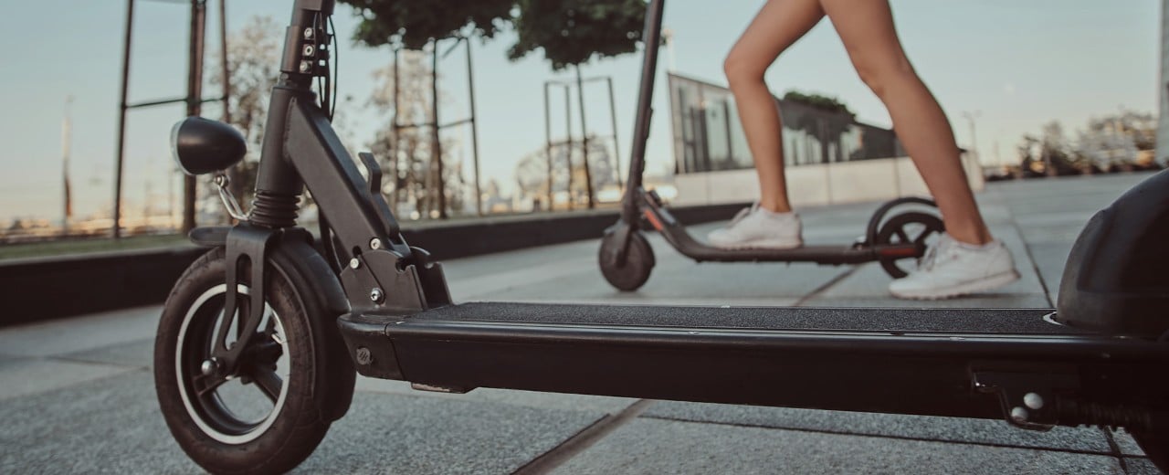 Elektrické kolobežky pripravené na jazdu po meste. Na jednu z nich práve naskakuje žena chystajúca sa vyraziť.