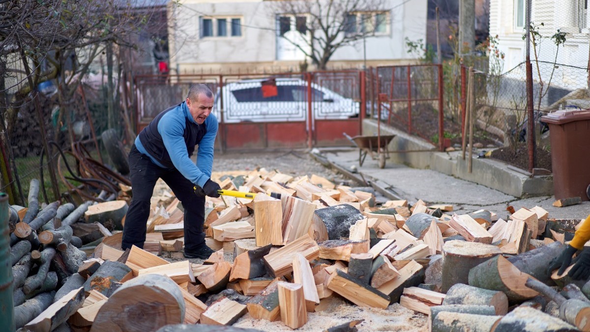 Muž rúbe drevo vo dvore domu.