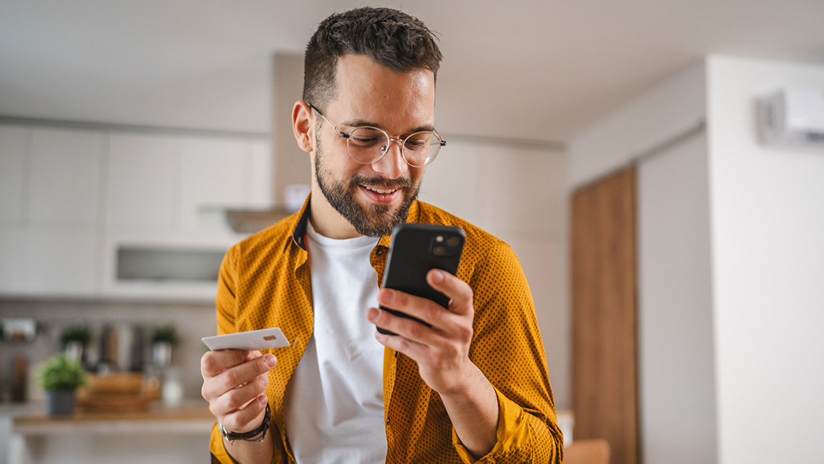 Muž nakupujúci online. V jednej ruke drží mobilný telefón a v druhej platobnú kartu.