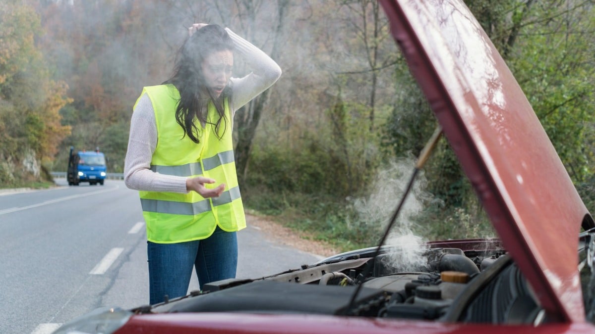 Žena v reflexnej veste sa chytá za hlavu, pretože jej dymí auto.