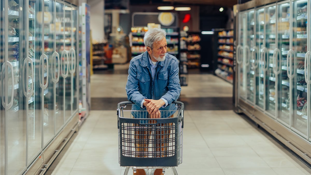 Starší muž nakupujúci v supermarkete. Pred sebou tlačí nákupný vozík.