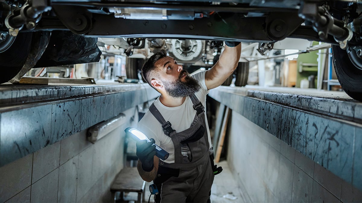 Mechanik pod autom v servise opravuje auto.