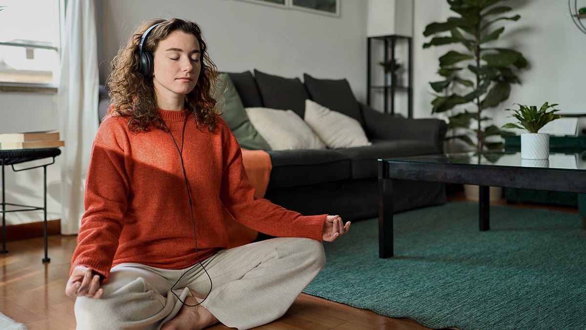 Mladá žena so slúchadlami na ušiach medituje v obývačke.