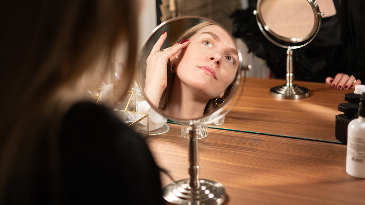 Žena pred zrkadlom venujúca sa svojej skincare rutine.