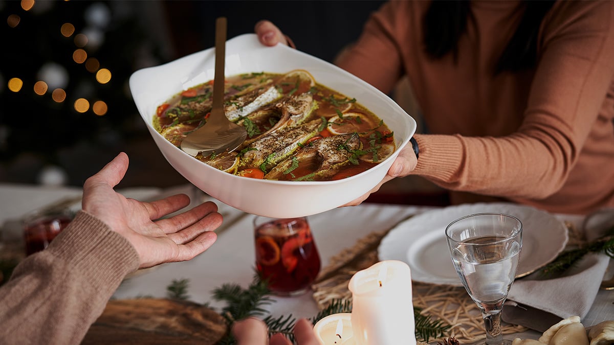 Žena pri štedrovečernom stole podáva jedlo mužovi.