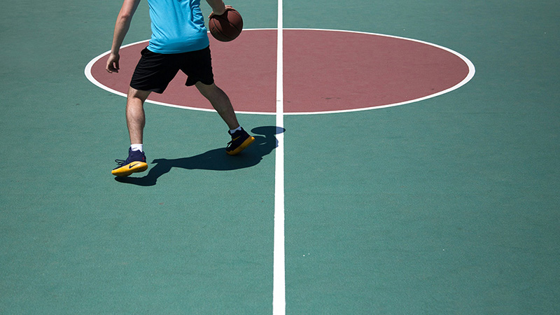 Muž dribluje basketbalovou loptou na ihrisku.
