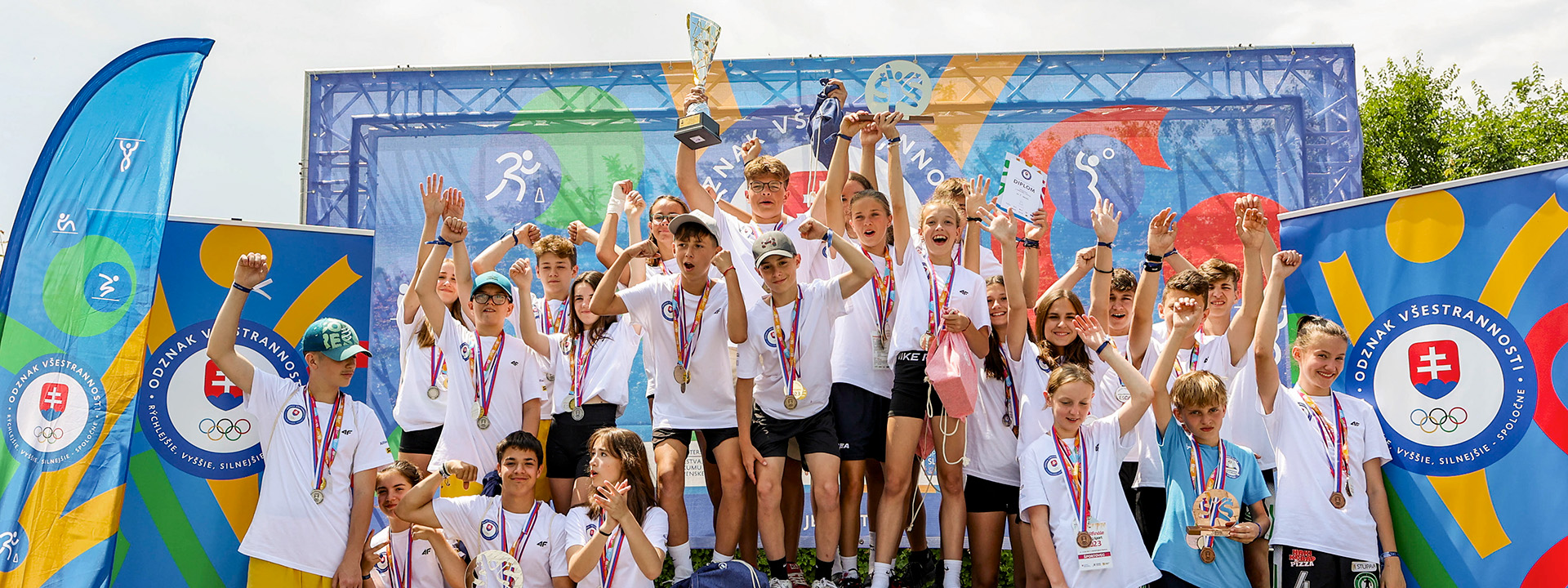Skupina detí s medailami a trofejami sa teší z výhry.