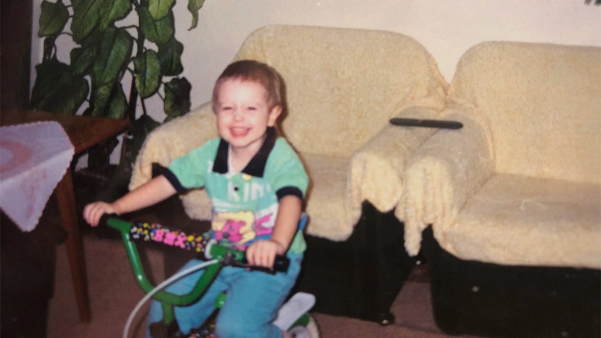 Mladý Martin Joppa, ešte ako dieťa, pózuje doma v obývačke na bicykli.
