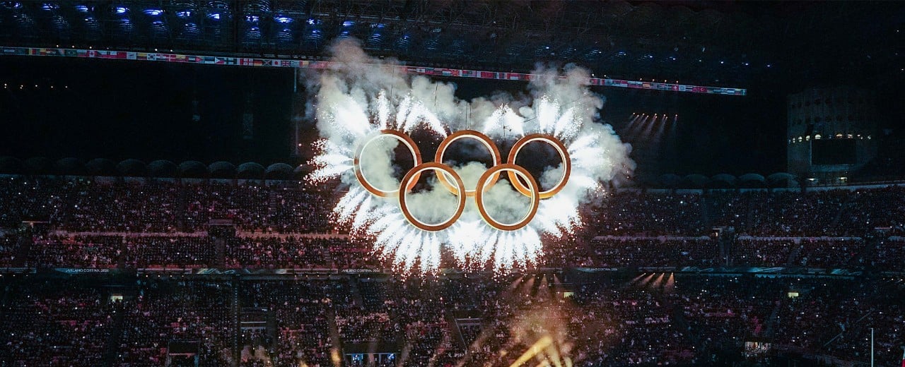 Olympijské kruhy ožiarené reflektormi a zadymené ohňostrojom