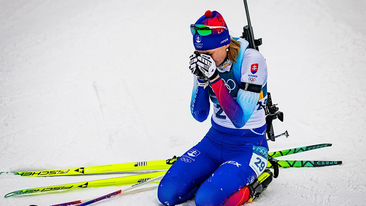 Biatlonistka Anastasiya Kuzmina vyčerpane sedí na snehu po náročných pretekoch.