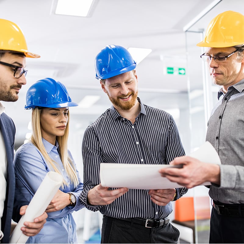 pracovnici stoja vo vyrobnej hale, v rukach maju papier