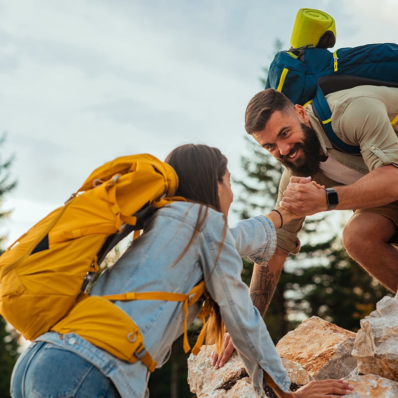 dvojica na skalach, muž pomáha žene dostať sa hore po kameňoch