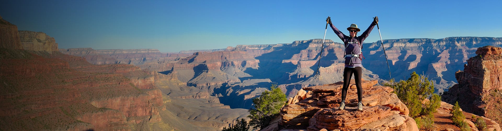 muž v Grand Canyon stoji na skale s rukami nad hlavou 