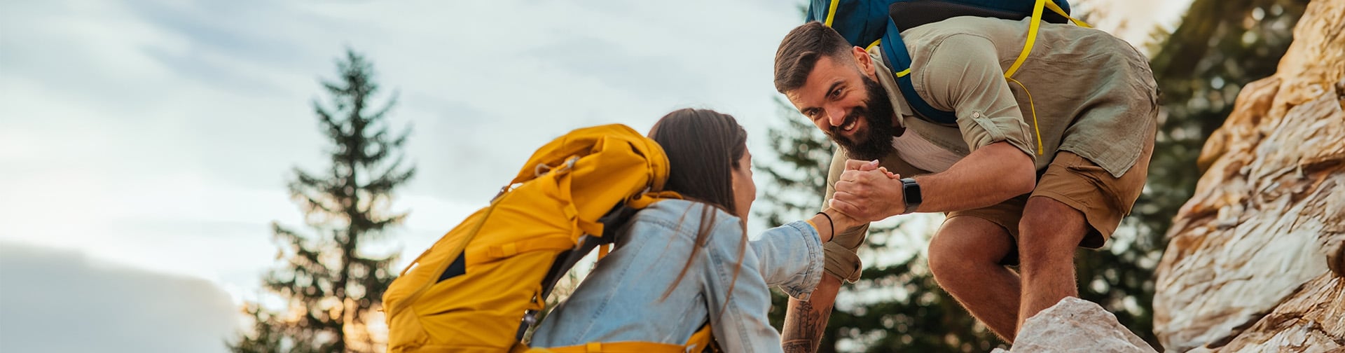 dvojica na skalach, muž pomáha žene dostať sa hore po kameňoch