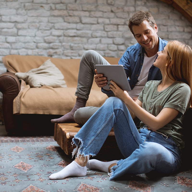 žena a muž sedia na zemi v obyvačke, zena drzi tablet v rukách