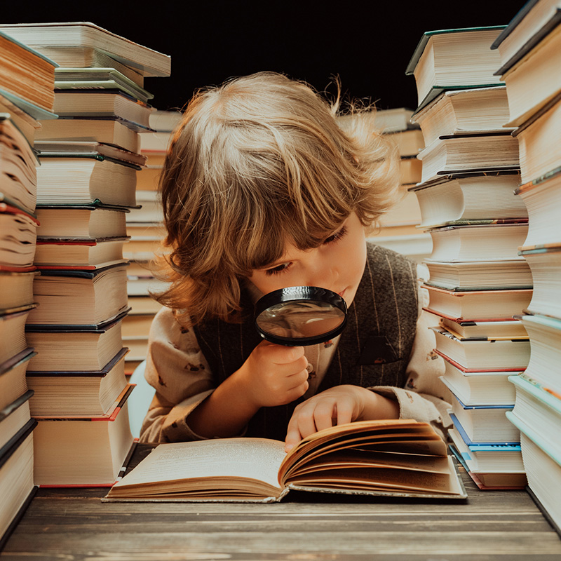 chlapec citajuci knihu, v ruke drzí lupu