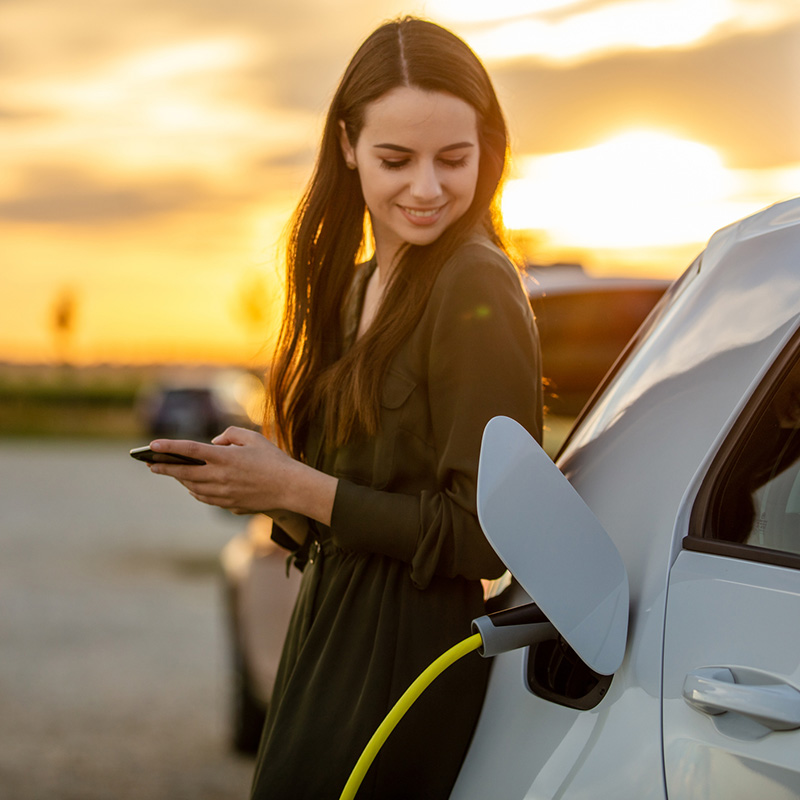 zena stojaca pri elektromobile, ktore nabíja