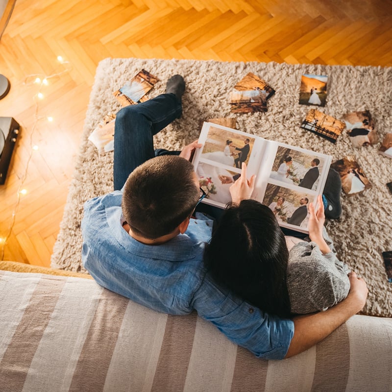 mladá dvojica muž a žena sedia na sedačke a pozerajú si fotografie, pohlad zvrchu