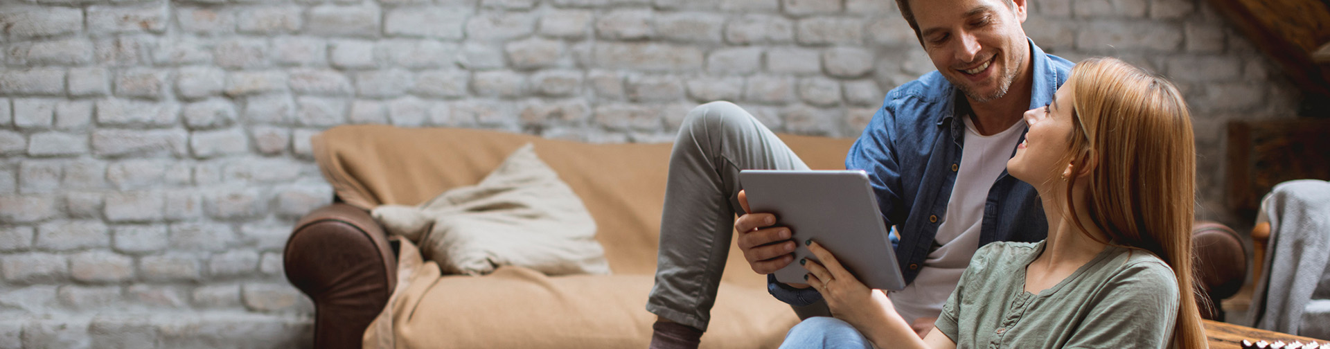 mladý pár sediaci v obývačke, pozerajú sa na seba, zena ma v ruke tablet