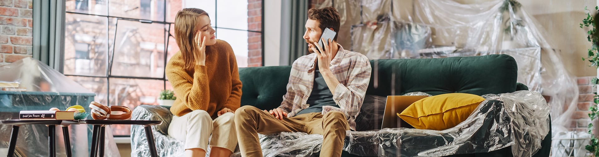 Dvaja ľudia telefonujú v byte s nábytkom zakrytým ochrannou fóliou počas riešenia škody v domácnosti.