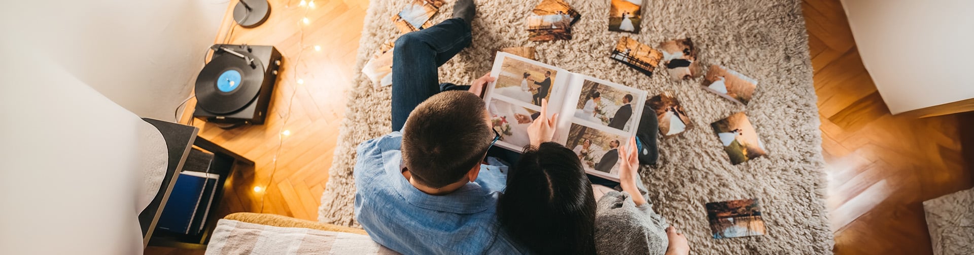 mladá dvojica muž a žena sedia na sedačke a pozerajú si fotografie, pohlad zvrchu