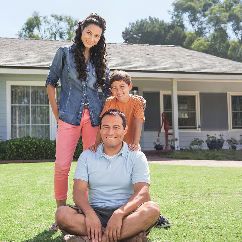 rodičia so syno pred domom, otec sedí na tráve, mama so synom sú za ním