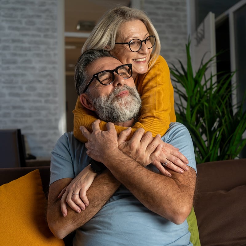 starší manželský pár, žena má ruky okolo ramien muža, muž drží ženu za ruky