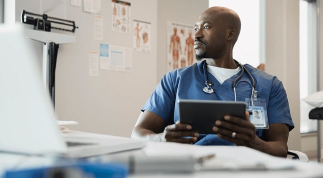 lekár afroameričan s tabletom v ruke sediaci v ordinacii
