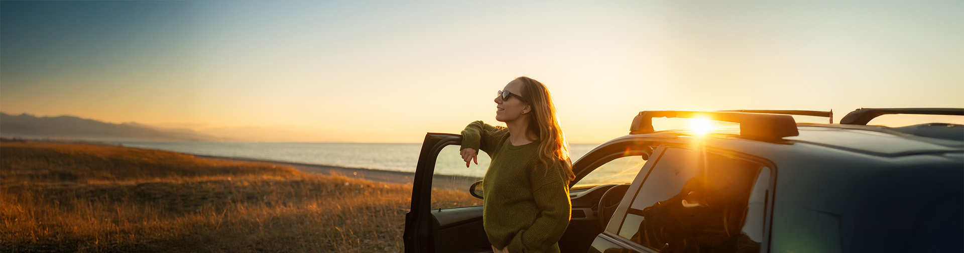 zapad slnka a zena stojaca pri dverach otvoreneho auta