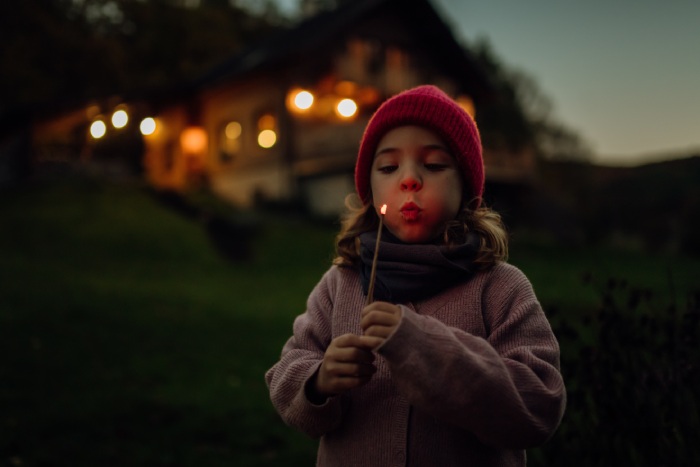 Dievča s horiacou paličkou v ruke stojí pred domom