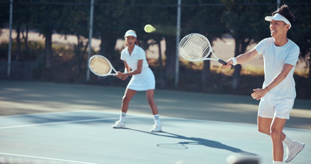 Dvaja hráči tenisu hrajú spoločne. Jeden z nich triafa do loptičky.